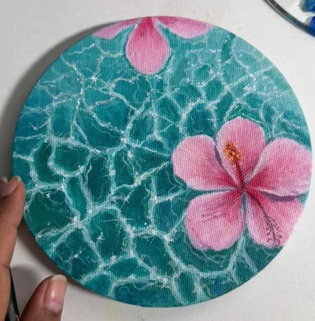 Pink hibiscus flowers float over turquoise water traced with shimmering ripples.
