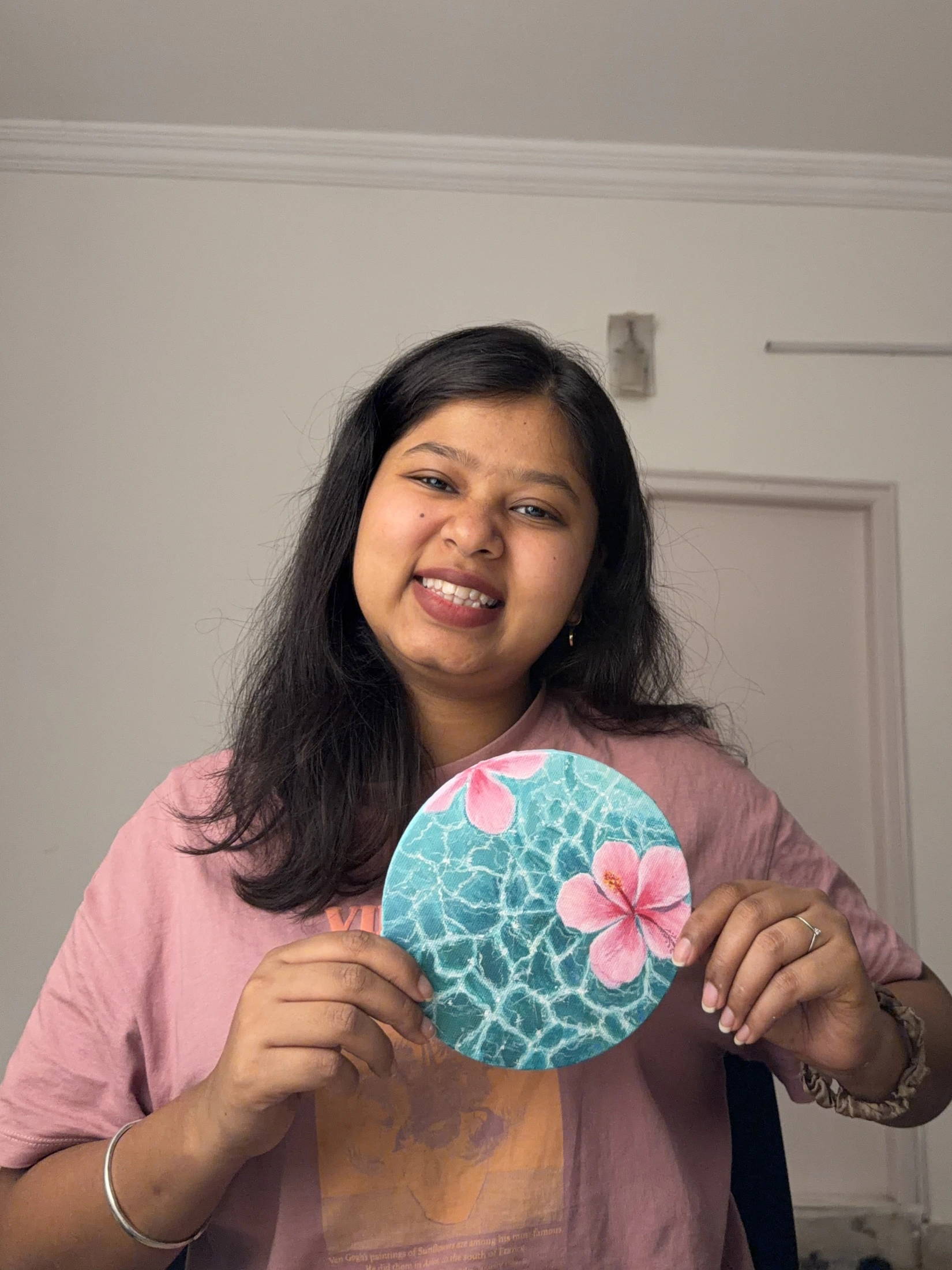 Isha Kamal holding a round turquoise painting with pink flowers