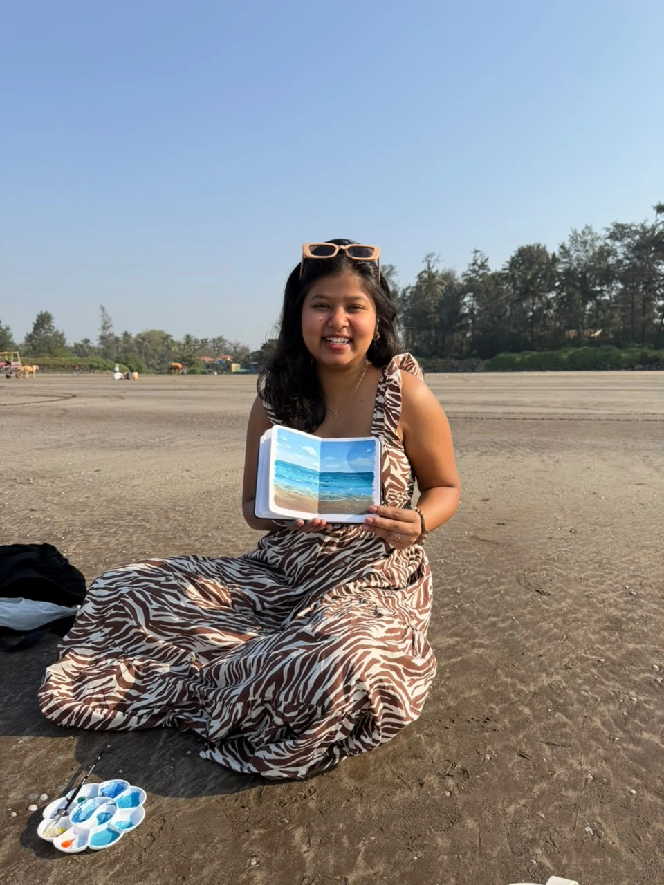 Isha outdoors holding an open painted sketchbook